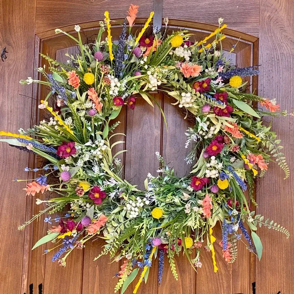 Farverig blomsterkrans på trædør, dekoreret med vilde blomster som lavendel, margueritter og grønne blade. Perfekt til sommerdekoration.