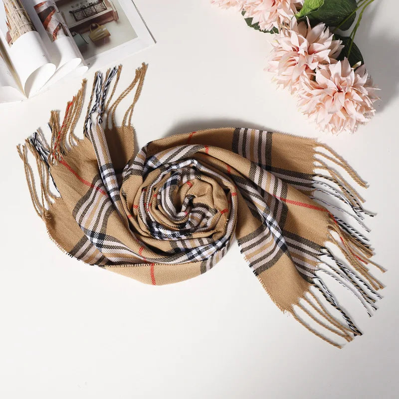 Beige ternet tørklæde med frynser på hvid baggrund ved siden af lyserøde blomster og åben bog. Elegant modeaccessory til efterår og vinter.