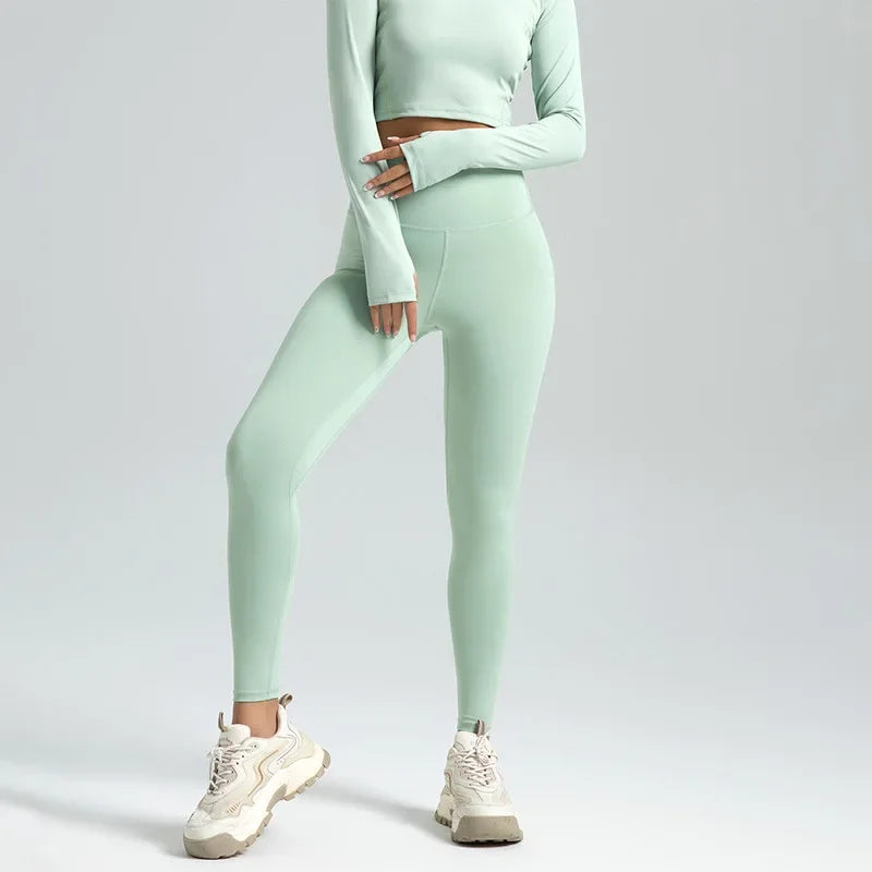 Kvinde iført lysegrønne leggings og matchende top, poserer med hvide sneakers. Moderne sportstøj, komfortabelt og stilfuldt til træning.