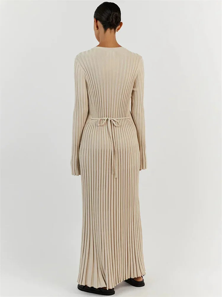 Kvinde iført lang, beige ribstrikket kjole set bagfra. Kjolen har bindebånd i taljen og lange ærmer. Elegant og minimalistisk design.