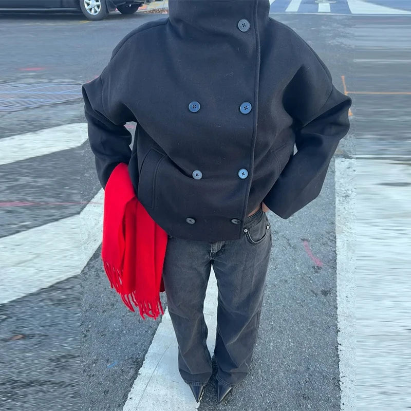 Person iført sort jakke og jeans står på gaden med rød tørklæde i hånden. Urban mode, vintertøj, street style.