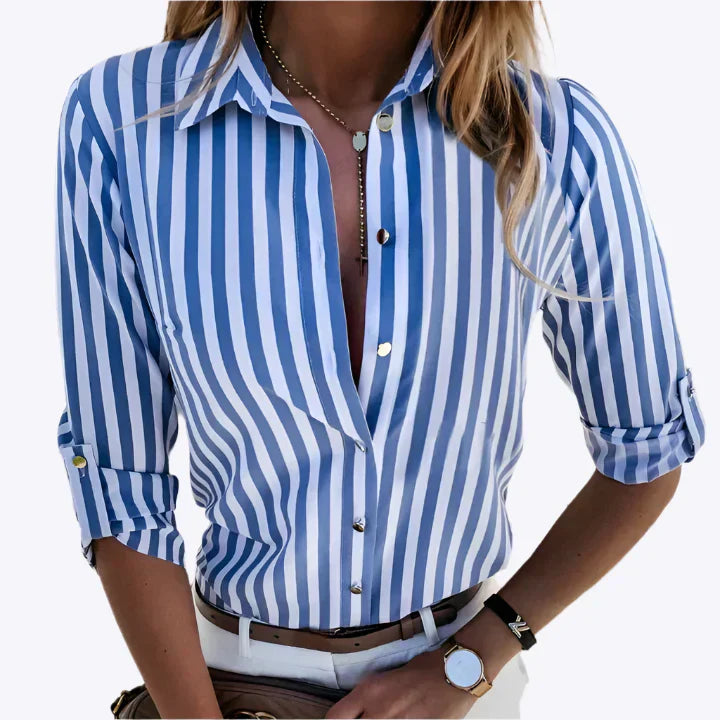 Kvinde iført blå-hvid stribet skjorte med opknappede ærmer, guldknapper og smykker. Moderne mode, stilfuldt outfit, casual elegance.