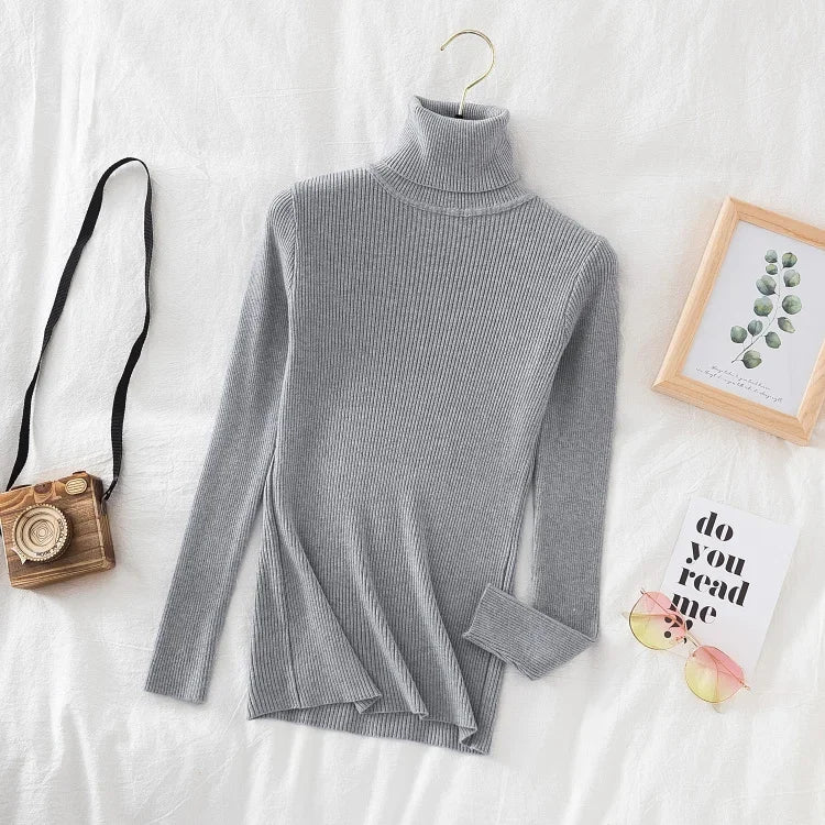 Grå rullekrave sweater i ribstrik på hvid baggrund, ved siden af vintage kamera, billedramme og bog. Stilfuldt vintertøj, mode til kvinder.