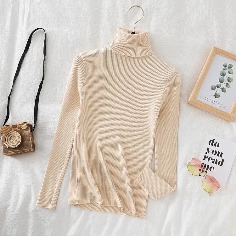 Beige rullekrave sweater på hvid baggrund med kamera, solbriller og plantebillede. Stilfuld, moderne mode til efterår og vinter.