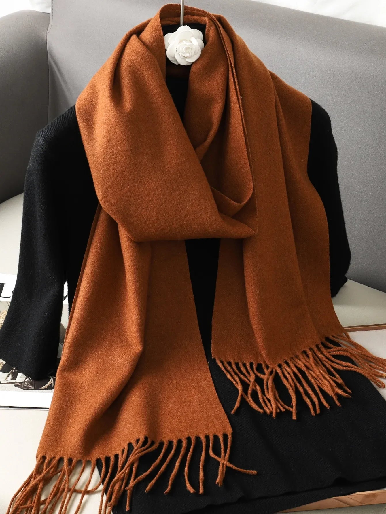 Brun uldskjerf med frynser på sort baggrund, elegant og varm til vintermode. Perfekt tilbehør til stilfulde og komfortable outfits.