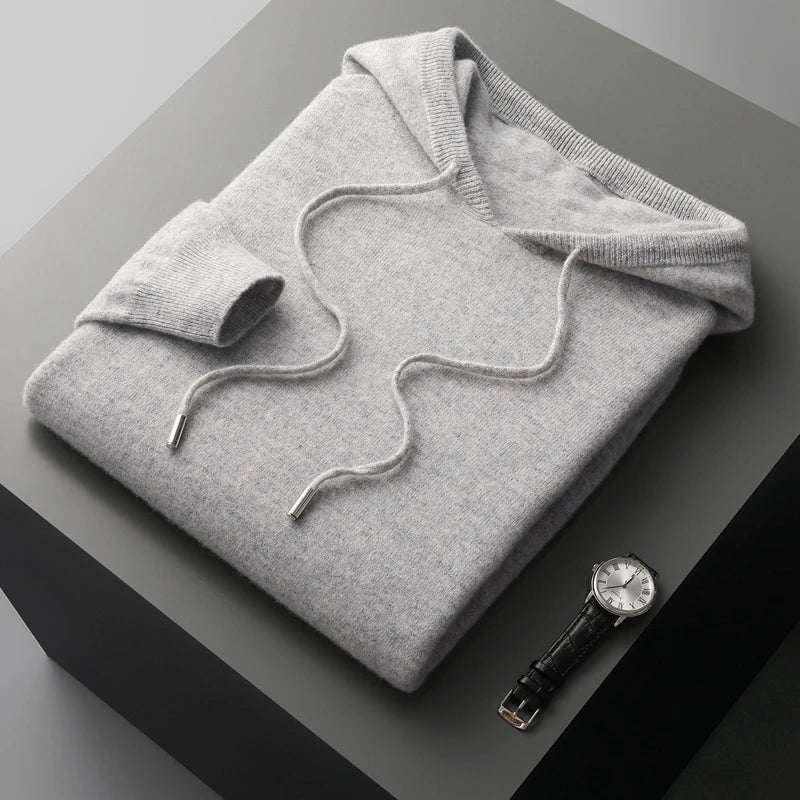 Grå cashmere hættetrøje foldet på bord, ved siden af sort læderrem ur. Luksuriøs striktrøje, stilfuldt tilbehør, moderne mode.