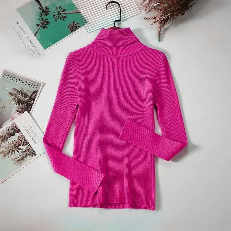 Lyserød rullekravebluse i ribstrik på hvid baggrund, omgivet af magasiner og tørrede blomster. Perfekt til efterårsmode og stilfulde outfits.