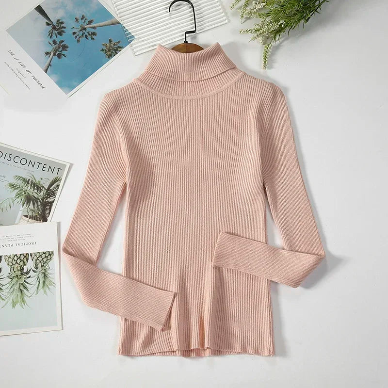 Lyserød ribstrikket rullekravetrøje på hvid baggrund, omgivet af blade og magasiner. Perfekt til efterårsmode og stilfulde outfits.