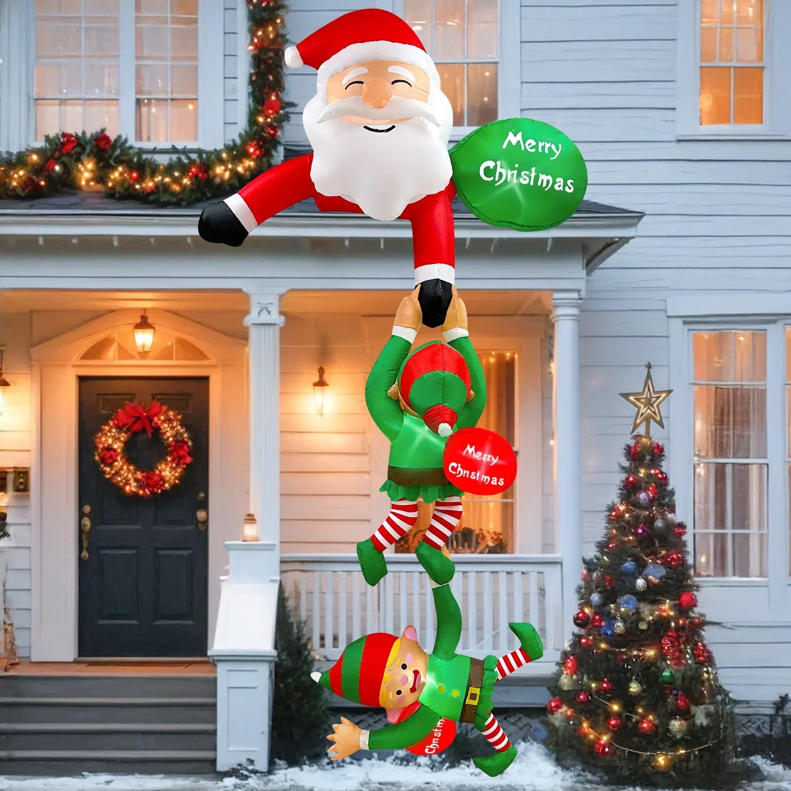 Oppustelig julemand og nisser dekoration foran hus, juletræ med lys, Merry Christmas skilt, festlig udendørs julepynt, vinterferie stemning.
