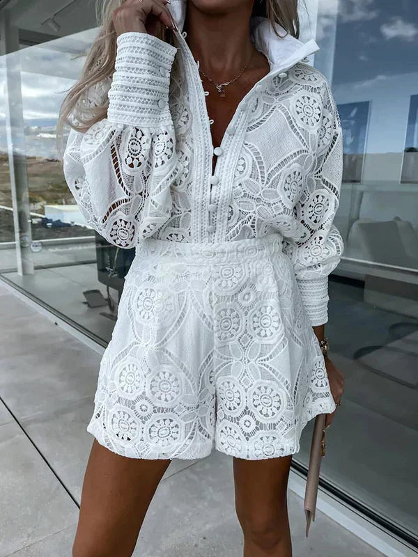 Kvinde iført hvidt, blonderet sæt med lange ærmer og shorts, stående udendørs. Elegant sommermode, moderne design, stilfuldt outfit.