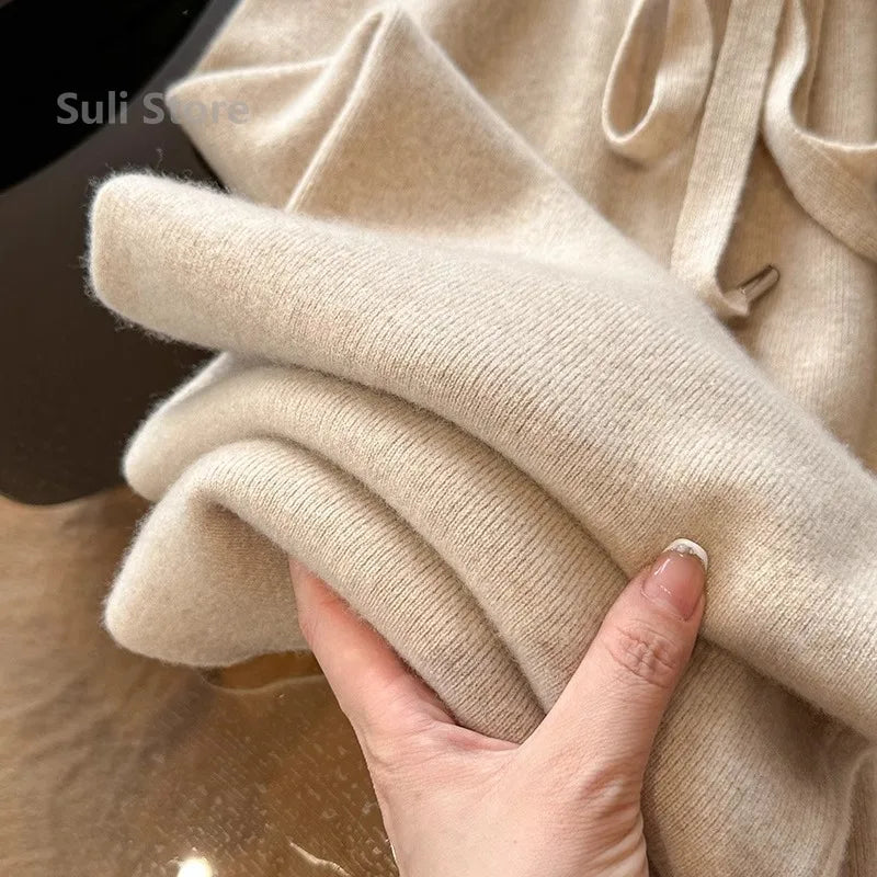 Hånd holder blød beige cashmere sweater, tæt tekstur, luksuriøst strik, vintermode, komfortabelt tøj, elegant design, varm beklædning.