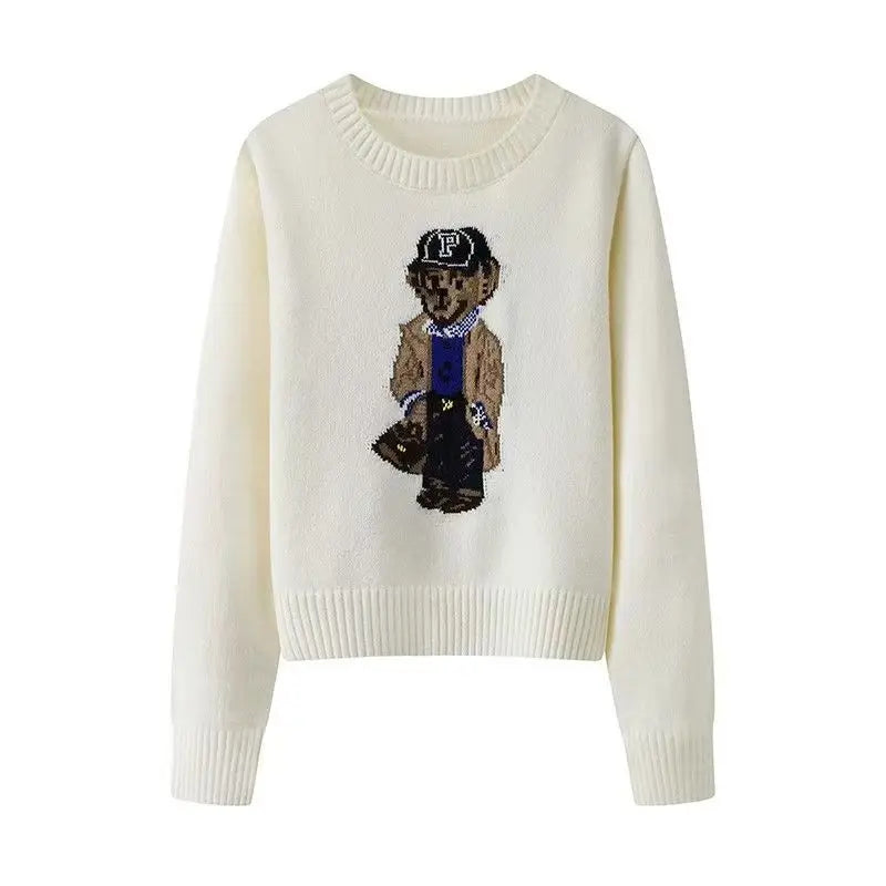 Hvid sweater med broderet bjørnemotiv iført trenchcoat og kasket. Trendy striktrøje til efterår og vinter. Unisex mode, casual stil.