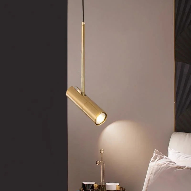 Guld pendellampe i moderne soveværelse, elegant belysning over natbord med kopper, minimalistisk design, stilfuld indretning.