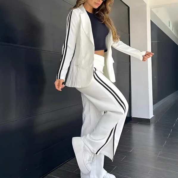 Kvinde iført hvidt jakkesæt med sorte striber, sort top og hvide sneakers. Moderne mode, sporty elegance, stilfuldt outfit til hverdag.