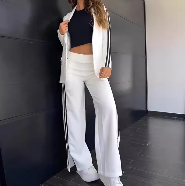 Ung kvinde iført hvidt jakkesæt med sorte striber, sort top og hvide sneakers. Moderne mode, stilfuldt outfit, minimalistisk design.