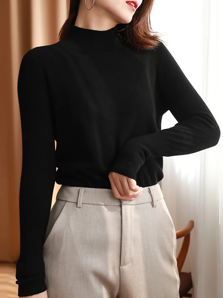 Kvinde iført sort højhalset sweater og beige bukser, stilfuldt outfit, moderne mode, minimalistisk design, elegant tøj til efterår og vinter.