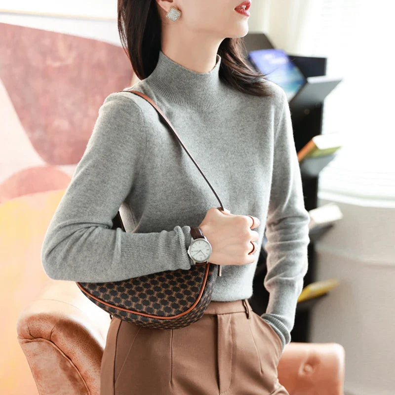 Kvinde i grå sweater med brun mønstret skuldertaske og ur, står i moderne interiør. Mode, stilfuldt tilbehør, elegant look.