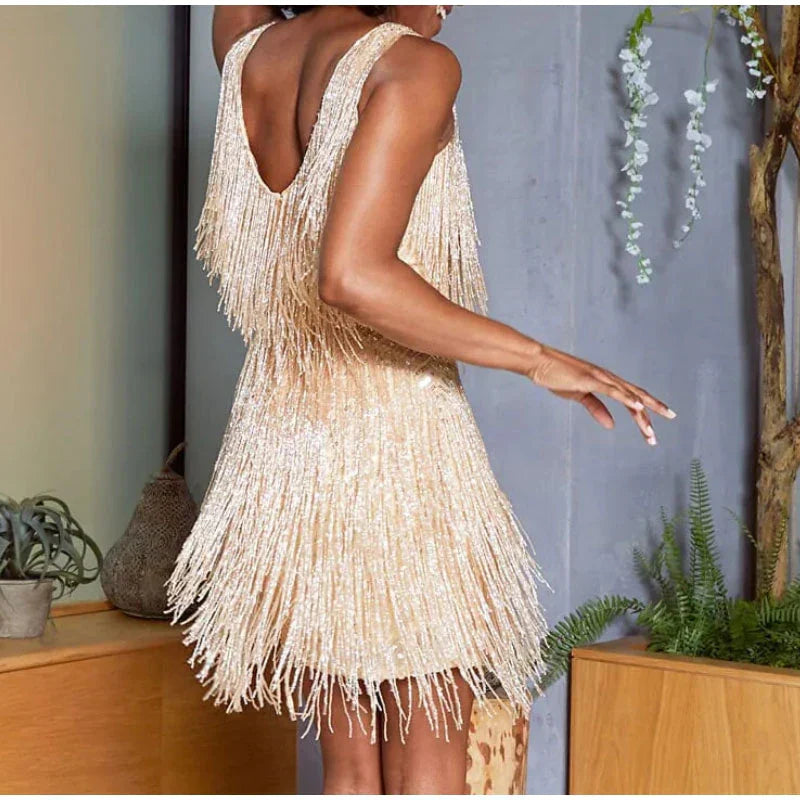 Kvinde i glitrende, frynsebeklædt cocktailkjole, elegant design, festkjole, beige nuance, moderne stil, indendørs, trendy mode.