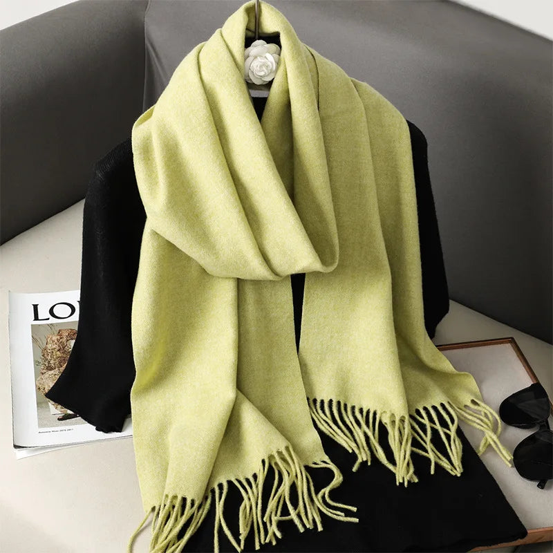 Lysegul uldhalsklæde med frynser på sort trøje, placeret på grå sofa. Perfekt til efterårsmode og vinterstil. Elegant og varm accessory.