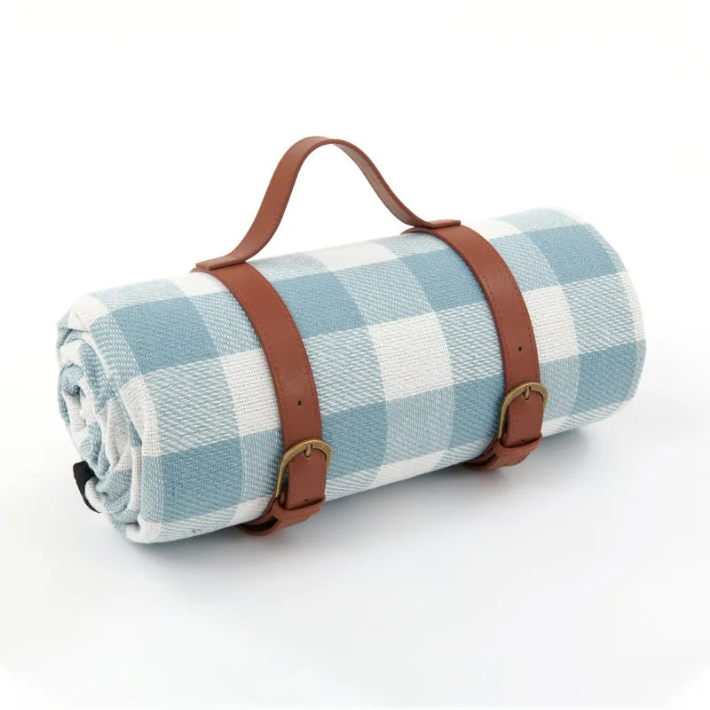 Blå-hvid ternet picnic tæppe med læderremme og håndtag, perfekt til udendørs brug. Praktisk og stilfuldt design til picnic og strandture.