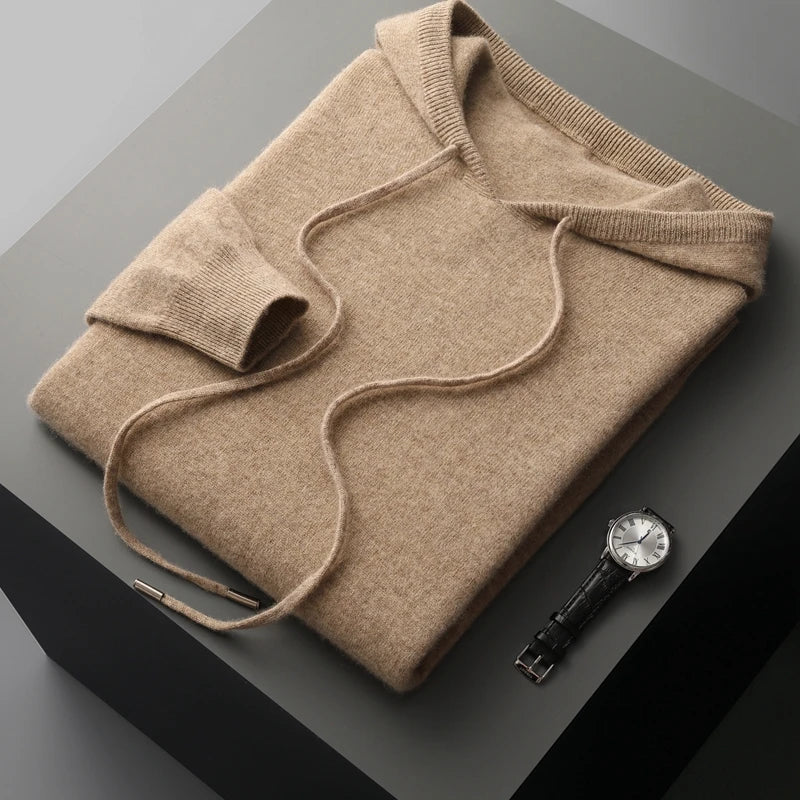 Beige cashmere hættetrøje foldet pænt på grå overflade ved siden af elegant sort læderrem ur. Luksuriøst tøj og tilbehør.