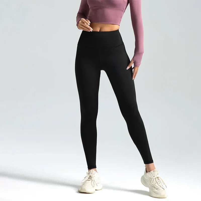 Kvinde iført sorte leggings og lyserød crop top, poserer mod grå baggrund. Komfortabelt sportstøj, ideelt til træning og yoga.