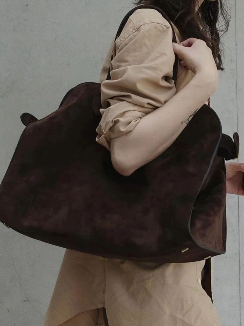 Kvinde med stor brun ruskindstaske, beige skjorte. Mode, tilbehør, stilfuld taske, moderne design, praktisk hverdagstaske.