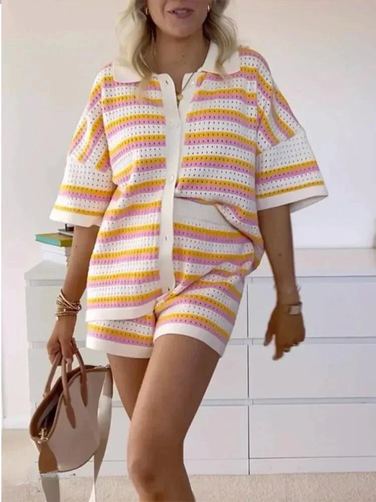 Kvinde iført stribet sommeroutfit med korte ærmer og shorts i pastelfarver, holder en brun taske. Moderne, afslappet stil til sommermode.