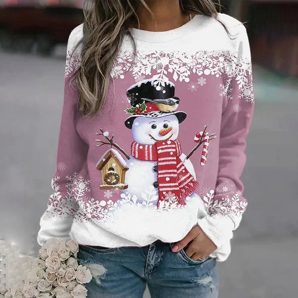 Kvinde iført lyserød sweater med snemand, sort hat, rødt halstørklæde og fuglehusmotiv. Perfekt til vintermode og juletema.
