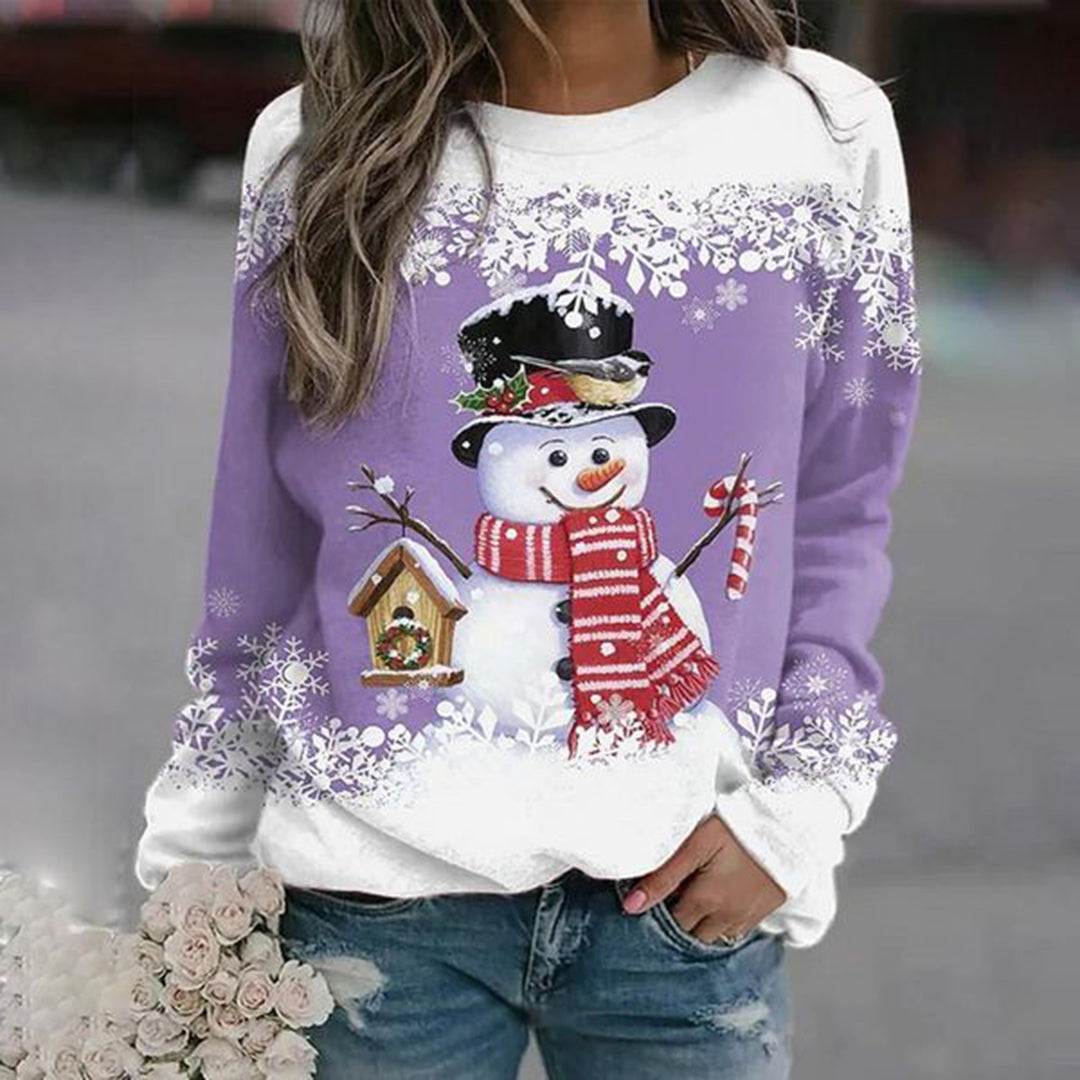 Kvinde iført lilla sweatshirt med snemand, sort hat, rødstribet halstørklæde og fuglehus. Perfekt til vintermode og juletema.