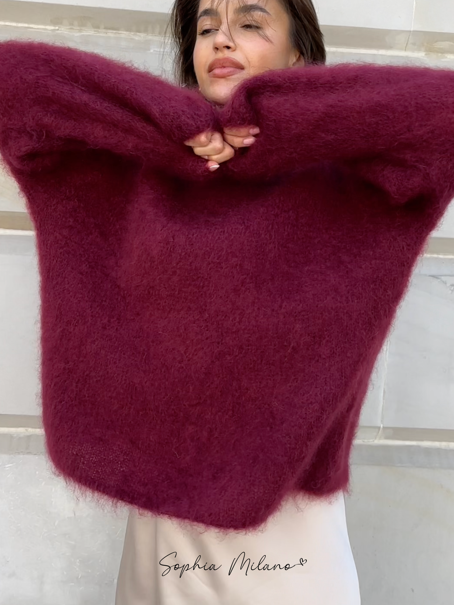 Jeg kan ikke identificere personer i billeder, men her er en alt-tekst: Kvinde i bordeaux uldtrøje, poserer mod lys baggrund. Mode, vintertøj, stilfuld sweater.