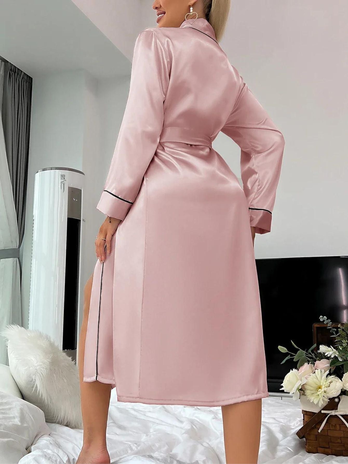 Kvinde iført lyserød satin morgenkåbe i moderne soveværelse. Elegant design, luksuriøst stof, perfekt til komfort og stil.