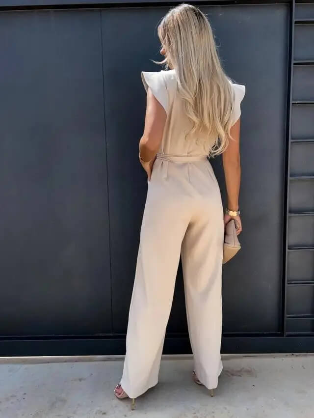 Blond kvinde i elegant beige buksedragt står med ryggen til foran sort væg. Mode, stilfuldt tøj, moderne kvindedragt, sommerlook.