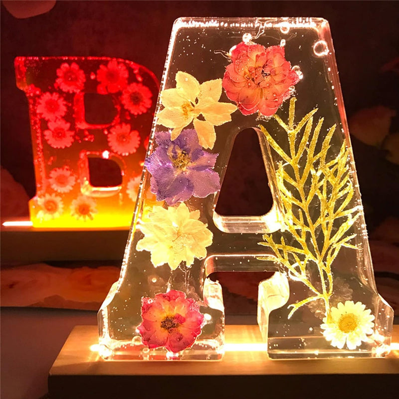 Bogstav A i gennemsigtig harpiks med indlejrede tørrede blomster og LED-lys. Dekorativt lysende bogstav til boligindretning og gaveidéer.