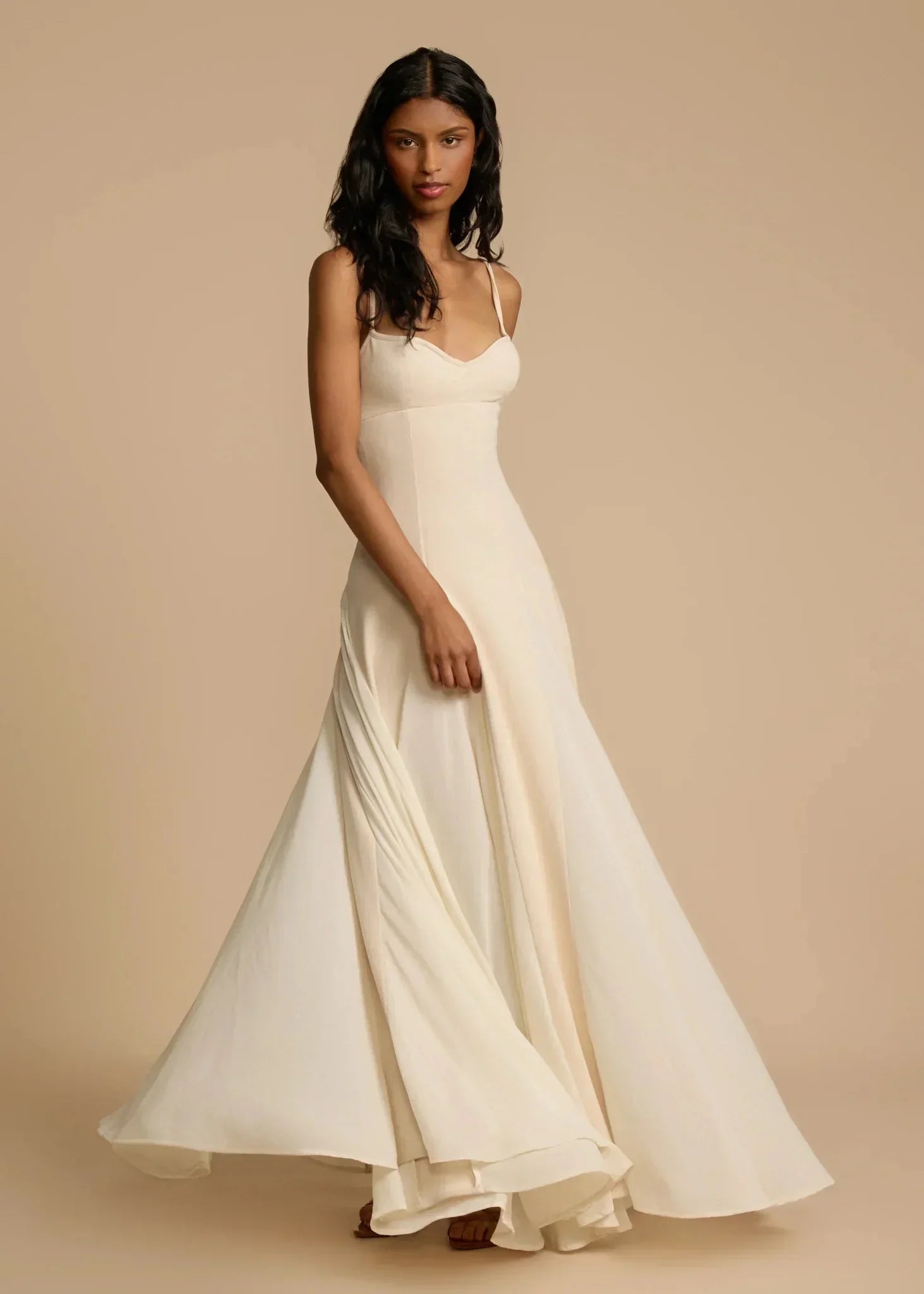 Kvinde i elegant, lang, beige aftenkjole med tynde stropper. Perfekt til formelle begivenheder. Stilfuldt og tidløst design.