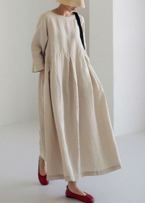 Kvinde i beige, løstsiddende maxikjole med lange ærmer, rød sko og stråhat. Minimalistisk mode, skandinavisk stil, komfortabelt tøj.