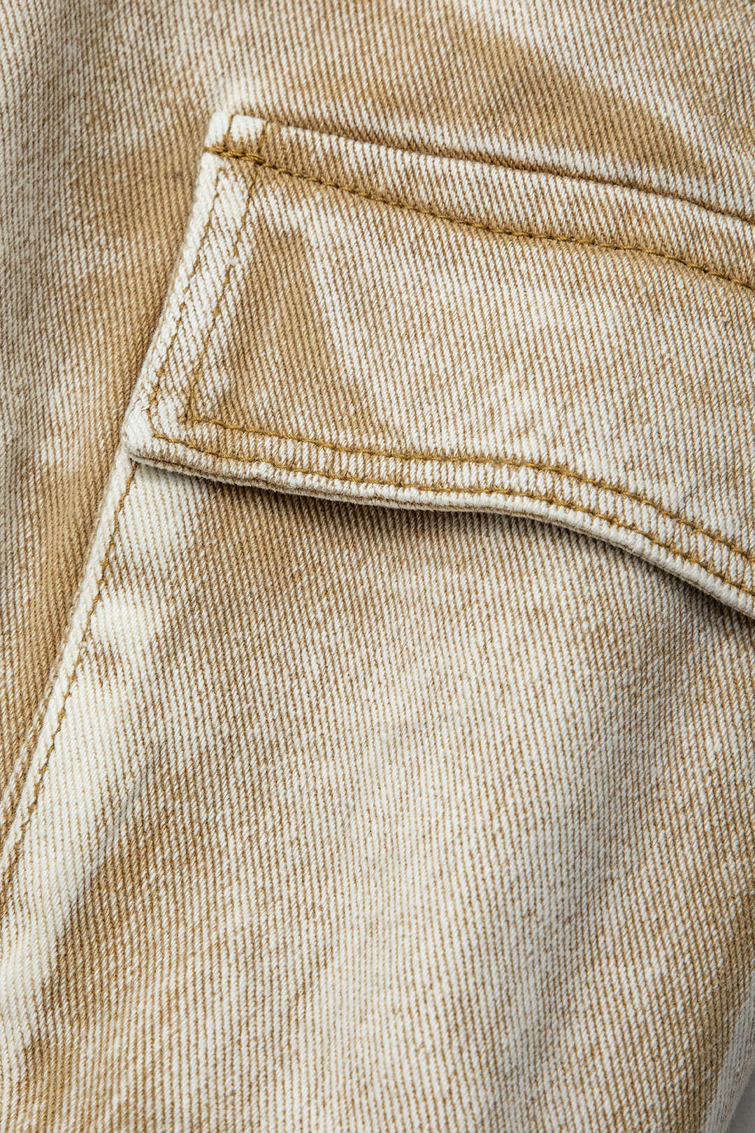 Beige denimstof med synlig lomme og syninger, nærbillede. Tekstur og detaljer i jeansmateriale. Mode, tekstil, tøjdesign.