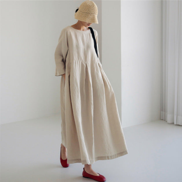 Kvinde i lang, beige kjole og stråhat i minimalistisk rum. Mode, skandinavisk stil, komfortabelt tøj, moderne design, røde sko.