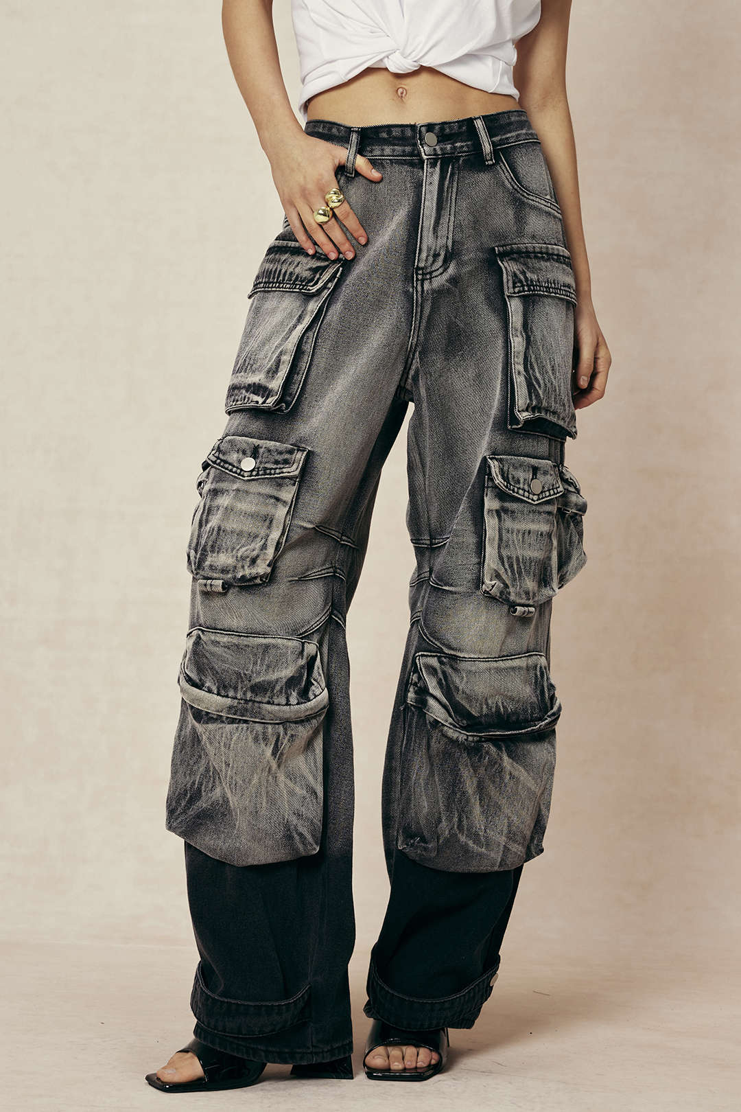Person iført grå cargo jeans med mange lommer og en hvid top. Trendy streetwear-stil, perfekt til modebevidste unge.