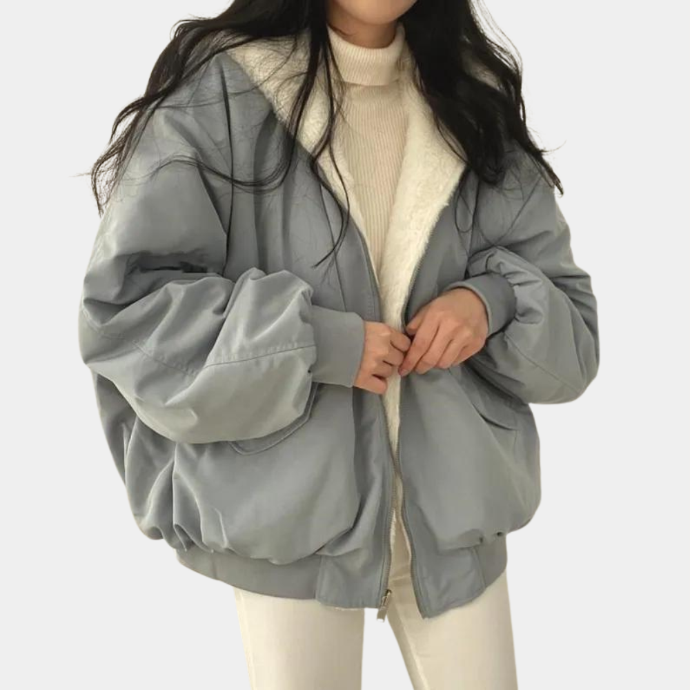 Kvinde iført lyseblå oversized jakke med hvid pelsfor, beige sweater og hvide bukser. Trendy vintermode, casual stil, komfortabelt tøj.