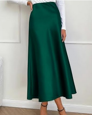 Kvinde iført lang, grøn A-formet nederdel og hvid bluse, står indendørs. Elegant mode, stilfuldt tøj, moderne kvindemode.