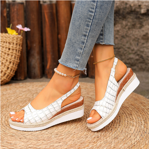 Dameben iført hvide kilehælsandaler med flettet mønster, kombineret med lyseblå jeans. Perfekt til sommermode og afslappet stil.