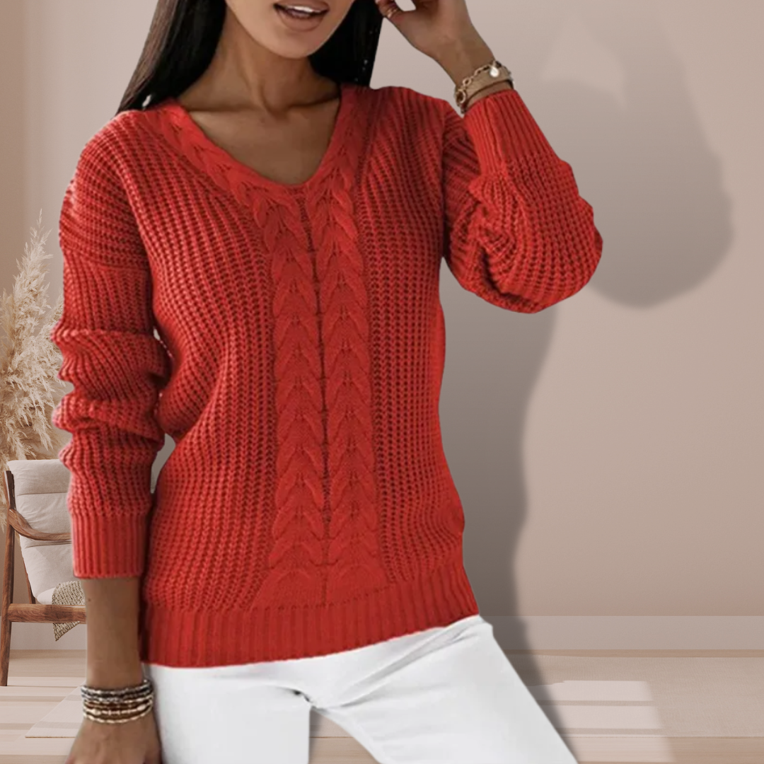 Kvinde iført rød striktrøje med V-hals og kabelstrikmønster, poserer i moderne stue. Mode, vintertøj, stilfuld sweater, damebeklædning.