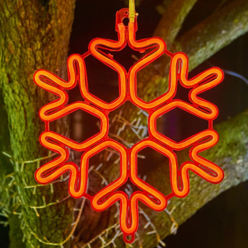 Rød neon snefnug dekoration hængende på træ, julebelysning, vinterpynt, lysende snefnug, festlig udendørs dekoration, julelys.