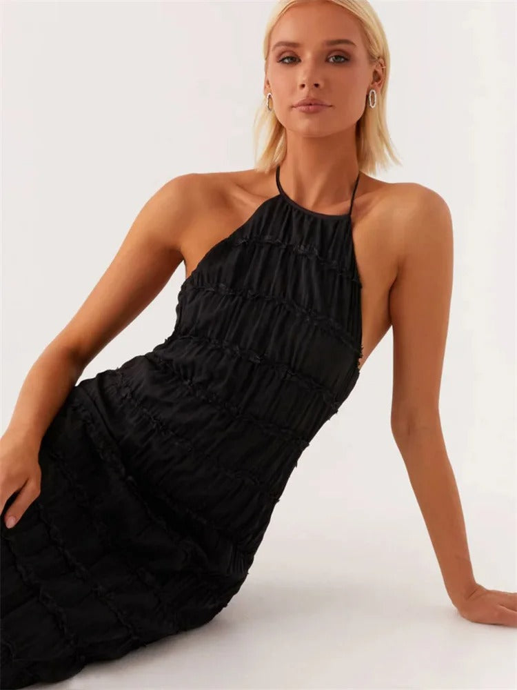 Kvinde i sort, ærmeløs kjole med halterneck, sidder afslappet. Elegant mode, moderne stil, minimalistisk design, perfekt til festlige lejligheder.