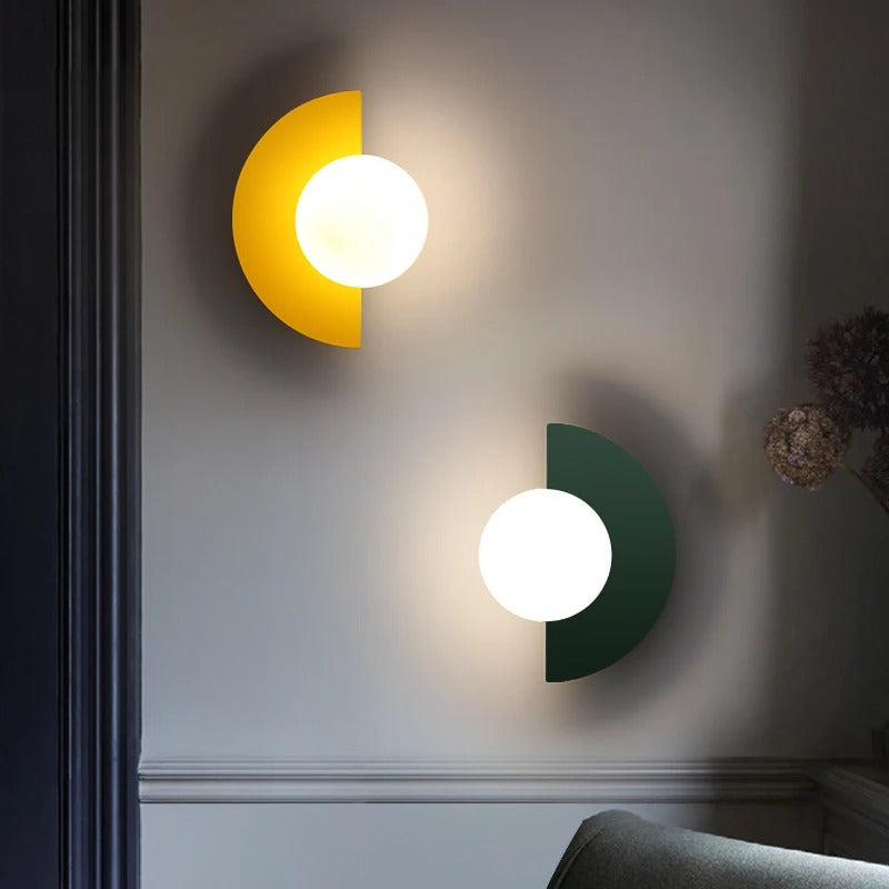 To væglamper i moderne design, en gul og en grøn, med halvcirkelformet baggrund og rund lyskilde, monteret på en væg i stue.