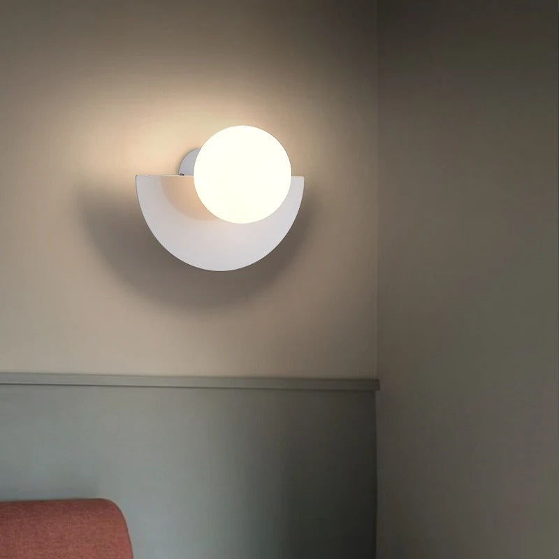 Moderne væglampe med rund, hvid skærm og minimalistisk design, monteret på en beige væg. Perfekt til stilfuld indretning og belysning.