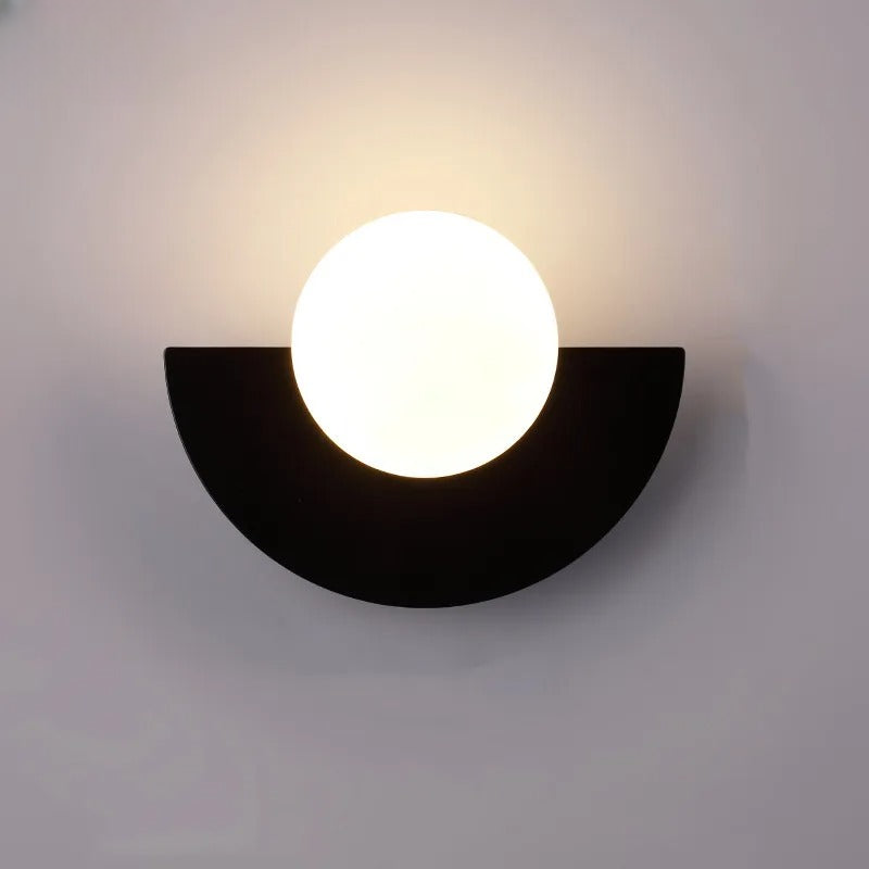 Moderne væglampe med halvcirkelformet sort base og rund hvid glaskuppel. Stilfuld belysning til hjemmet, minimalistisk design.