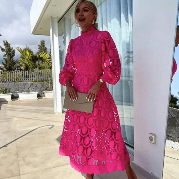 Kvindelig model i lyserød blondekjole står udendørs ved moderne bygning. Sommermode, elegant design, stilfuld kjole, kvindetøj.