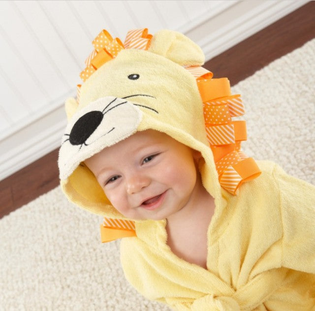 Baby iført gul løve-kostume med hætte og orange manke, smilende på tæppe. Sødt babytøj, dyrekostume, børnemode, indendørs leg.